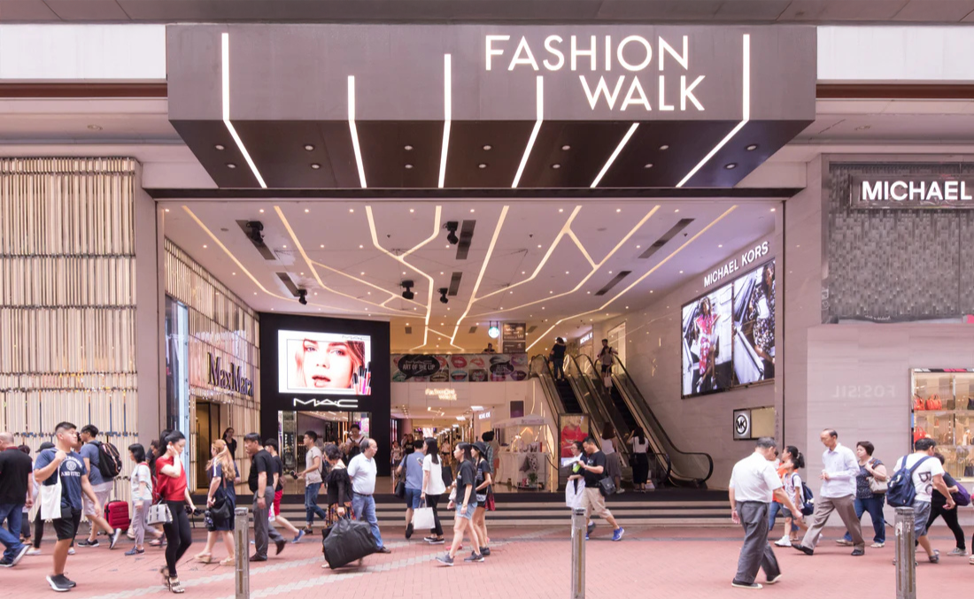 Fashion Walk mall entrance with people walking around, featuring brand logos like MAC and Michael Kors.